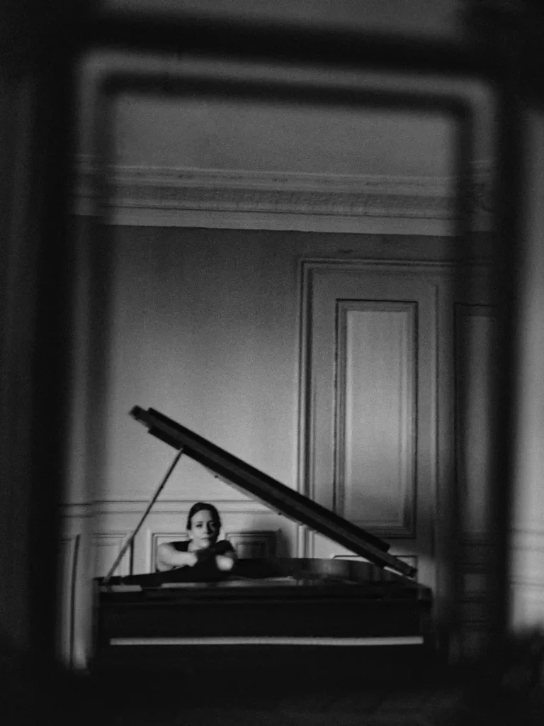 Portrait éditorial, d'une femme assise devant un piano, bras croisés posés sur l’instrument, regardant l’objectif.