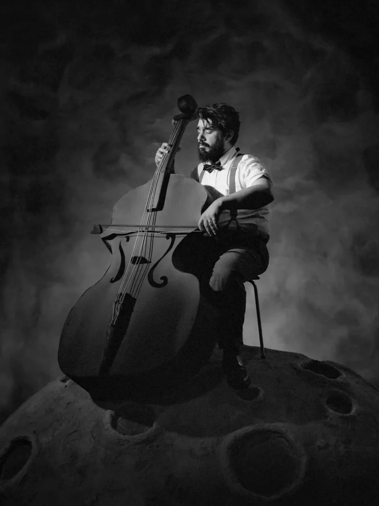 Photographie conceptuelle, musicien assis sur une planète, jouant de la contrebasse.