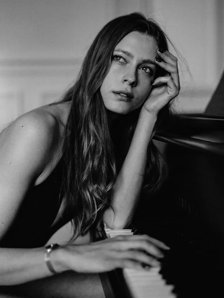 Femme assise devant un piano, regard tourné sur le côté, posture détendue.