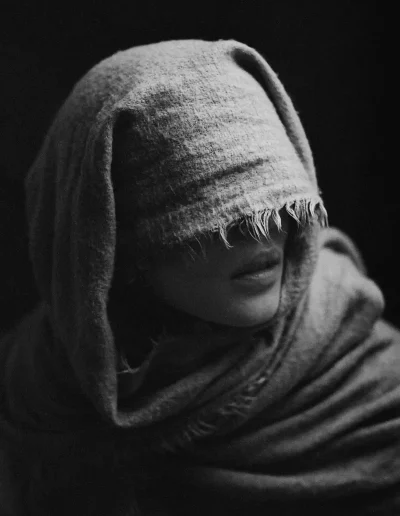 Femme en cadrage rapproché, bouche visible sous une couverture, fond sombre, éclairage frontal.