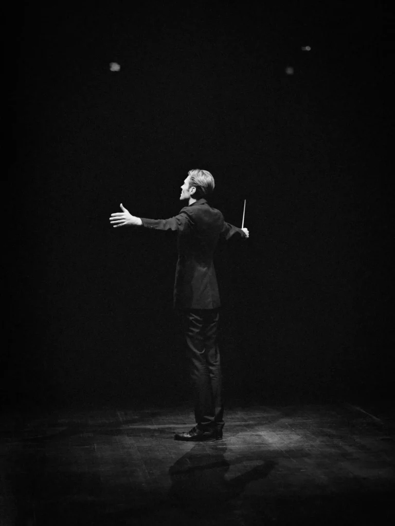 Portrait artistique d’un chef d’orchestre, posture expansive, noir intense, lumière focalisée.