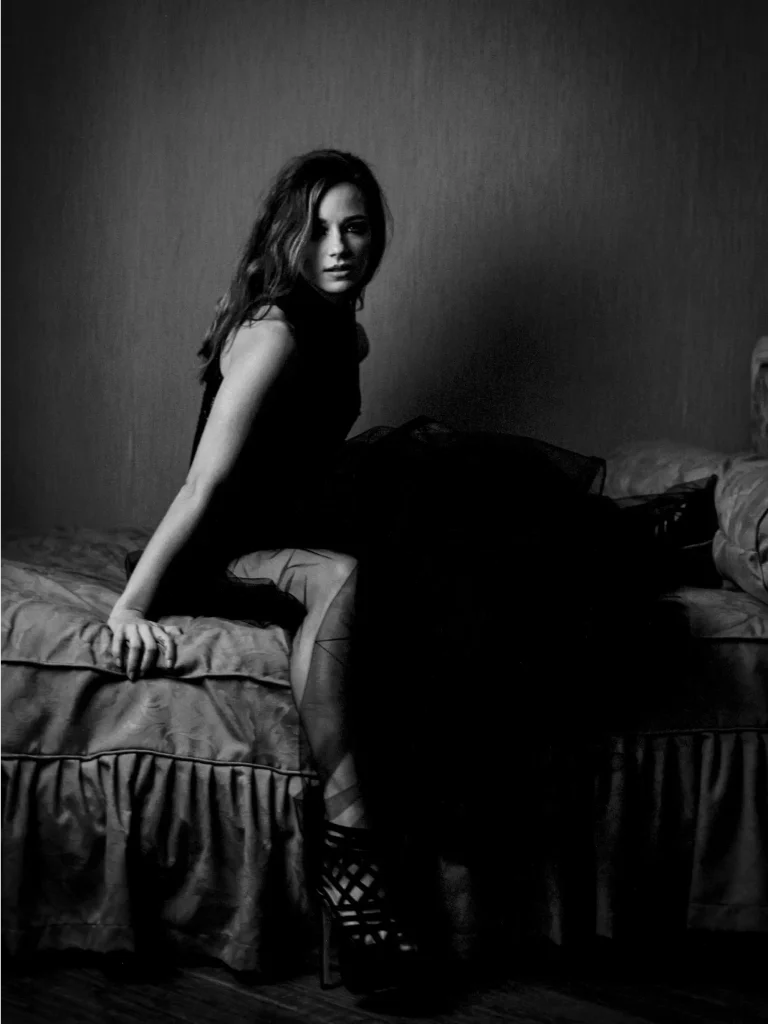 Portrait d'une femme posant sur un lit, regard vers l’objectif.